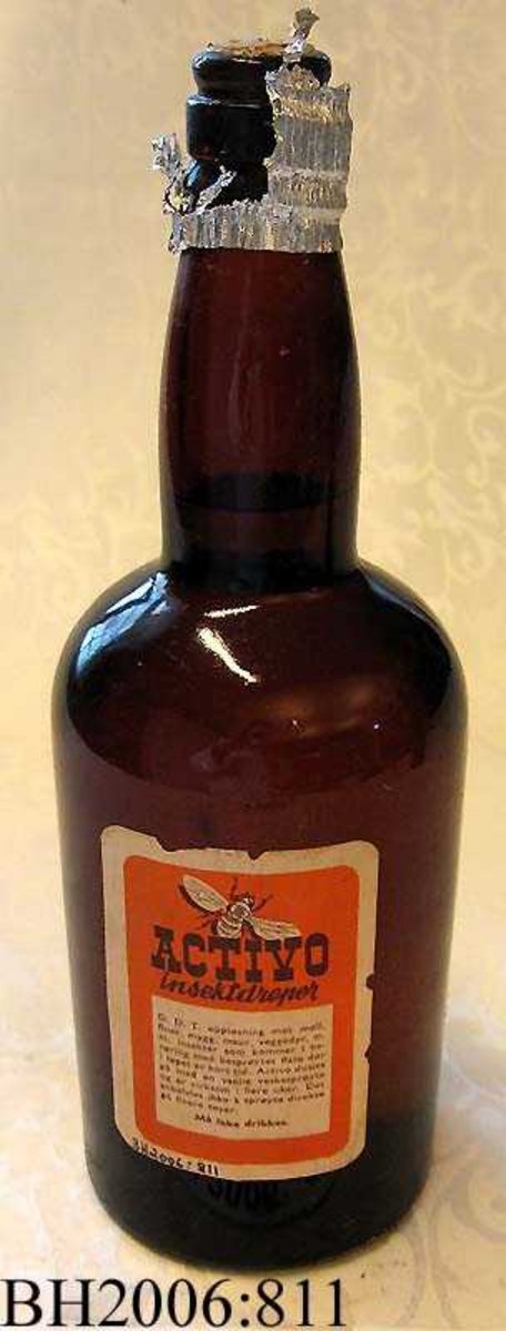 Flaske av brunt glass med activo insektdreper. Flasken er uåpnet og har en oransje og hvit etikett med informasjon om innholdet.