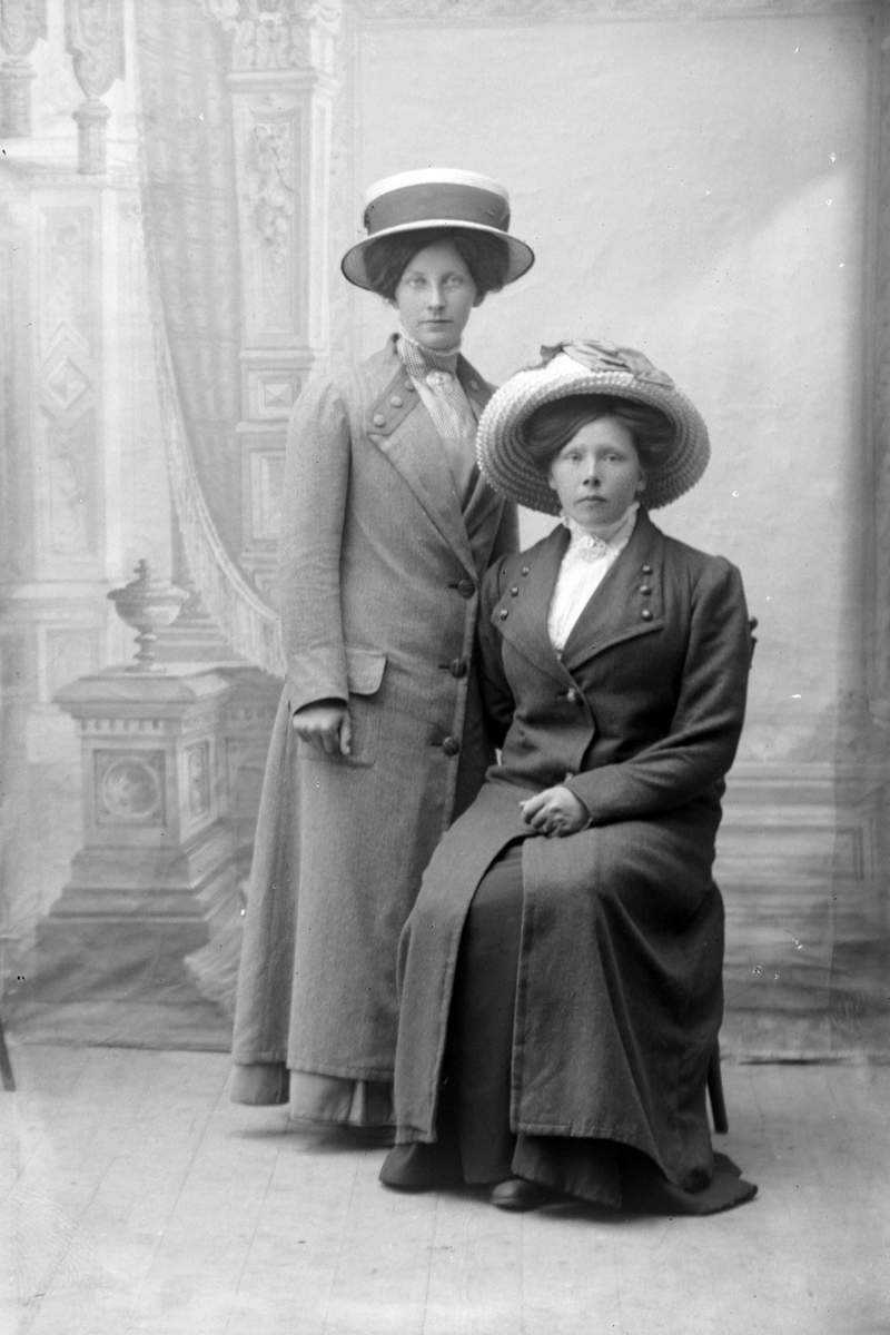 Studioportrett av to kvinner med hatter på hodet.
