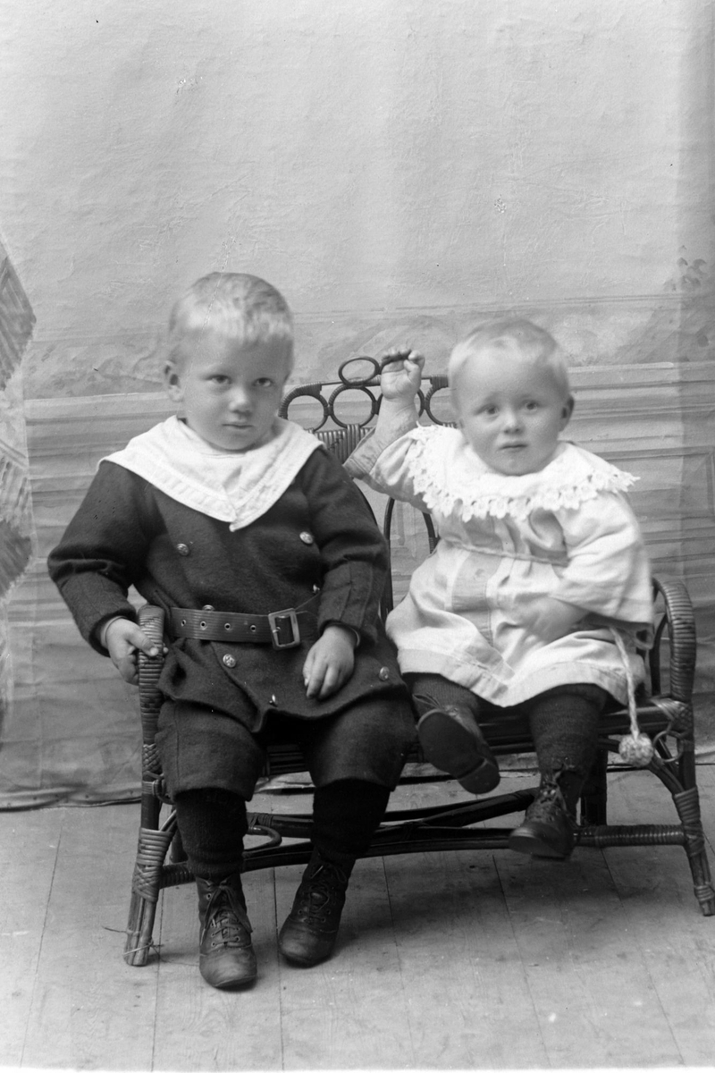 Studioportrett av to små barn i helfigur, muligens brødrene Jakob og Hjalmar Pedersen.