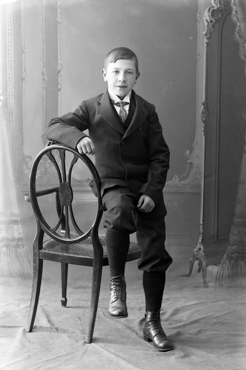 Studioportrett av en gutt som lener seg på en stol.