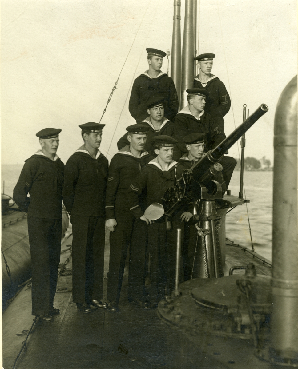 Delfinen. sjösatt 1915. Grupp av besättningen vid 37 mm kanonen, provisorisk [monterad], sedermera ersatt av 57 mm Ubkan (den första ubåtskanonen). Kanonen medtogs med hjälp av repet kring konen vid dykning.
Gåva dir. O. Almgren 2/4 1946.