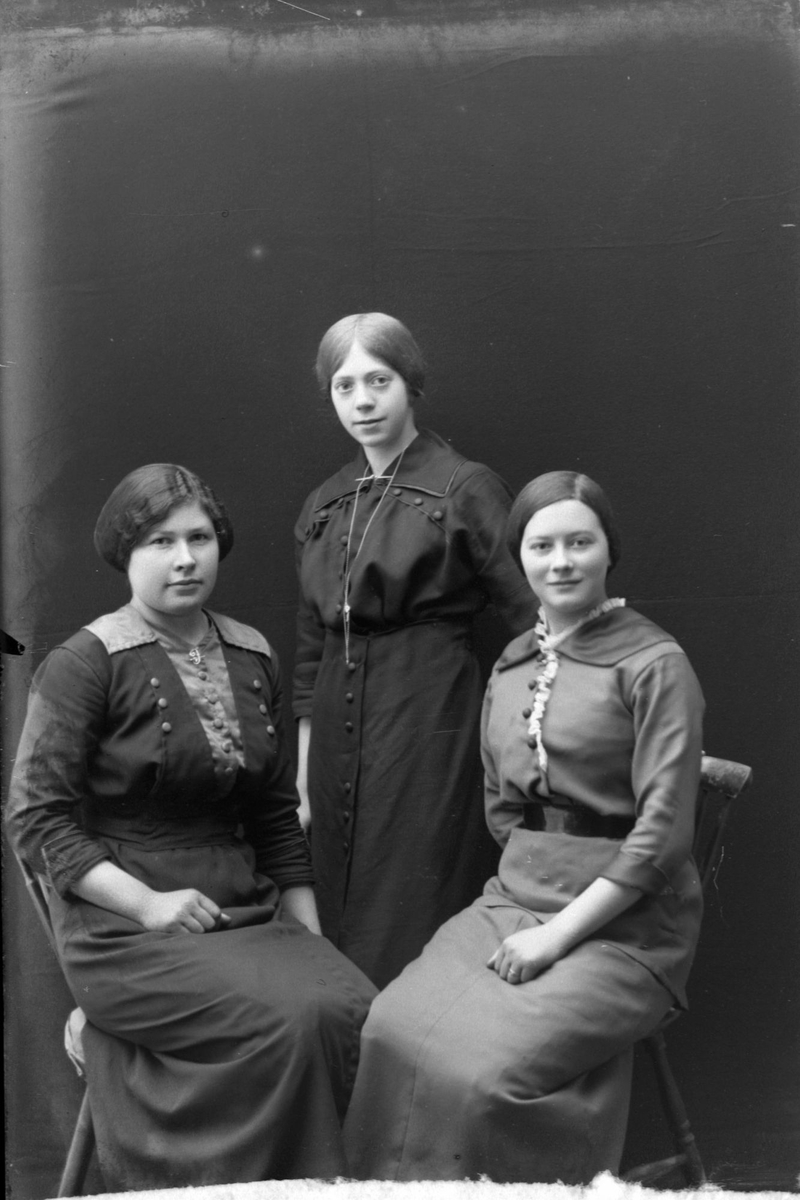 Studioportrett av to kvinner som sitter og én som står.