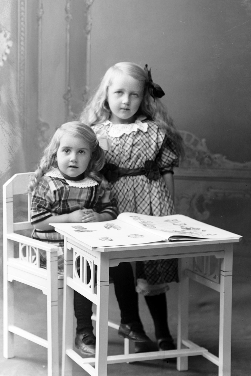 Studioportrett av to jenter ved et bord.