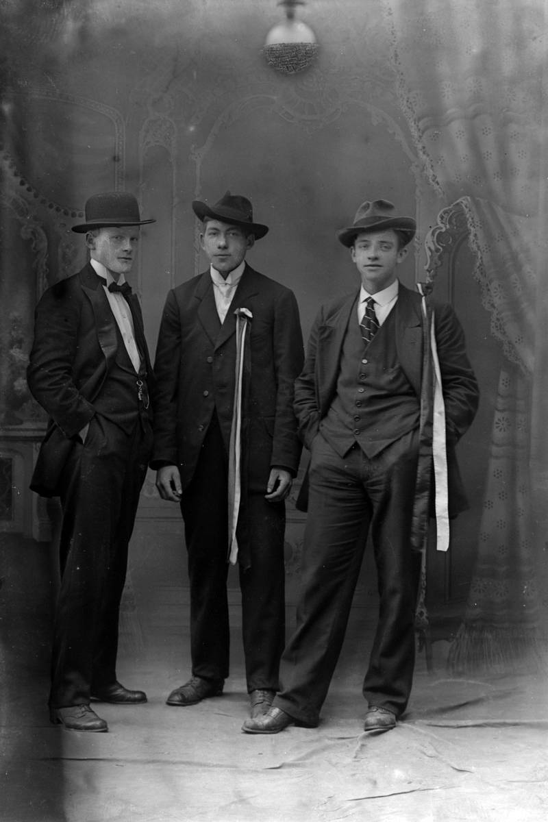 Studioportrett av tre menn, to av dem med sløyfer på brystet.