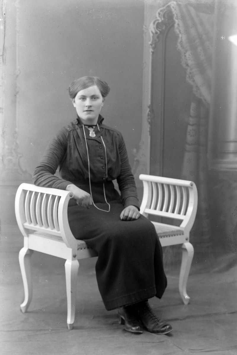 Studioportrett av en kvinne sittende på en benk.
