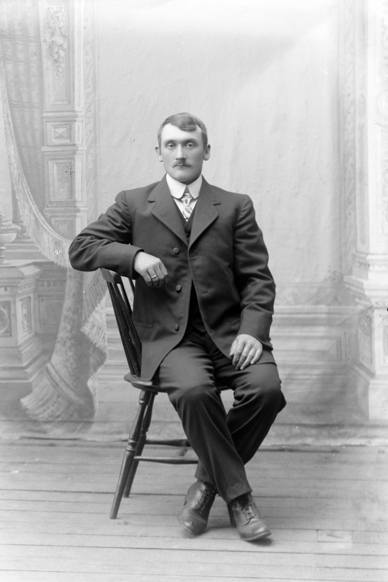 Studioportrett av en mann sittende på en stol.