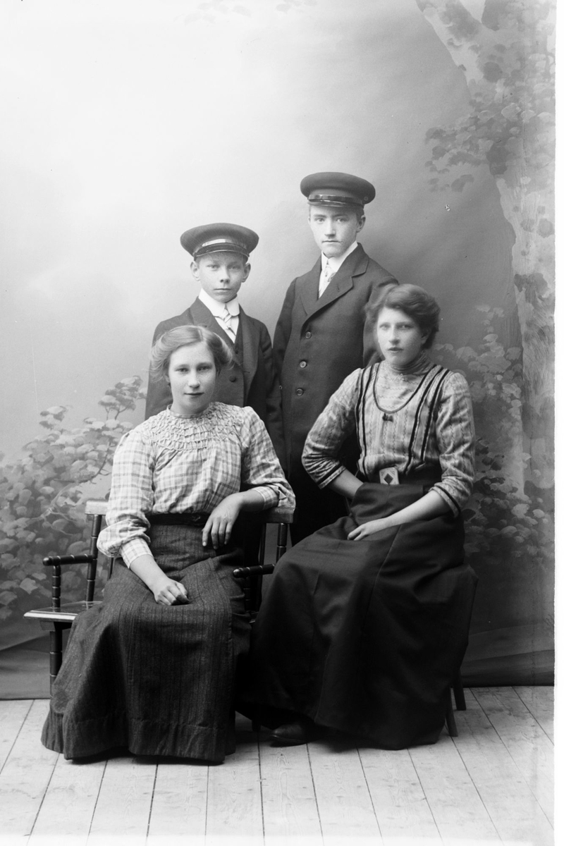 Studioportrett av to kvinner sittende foran to menn.