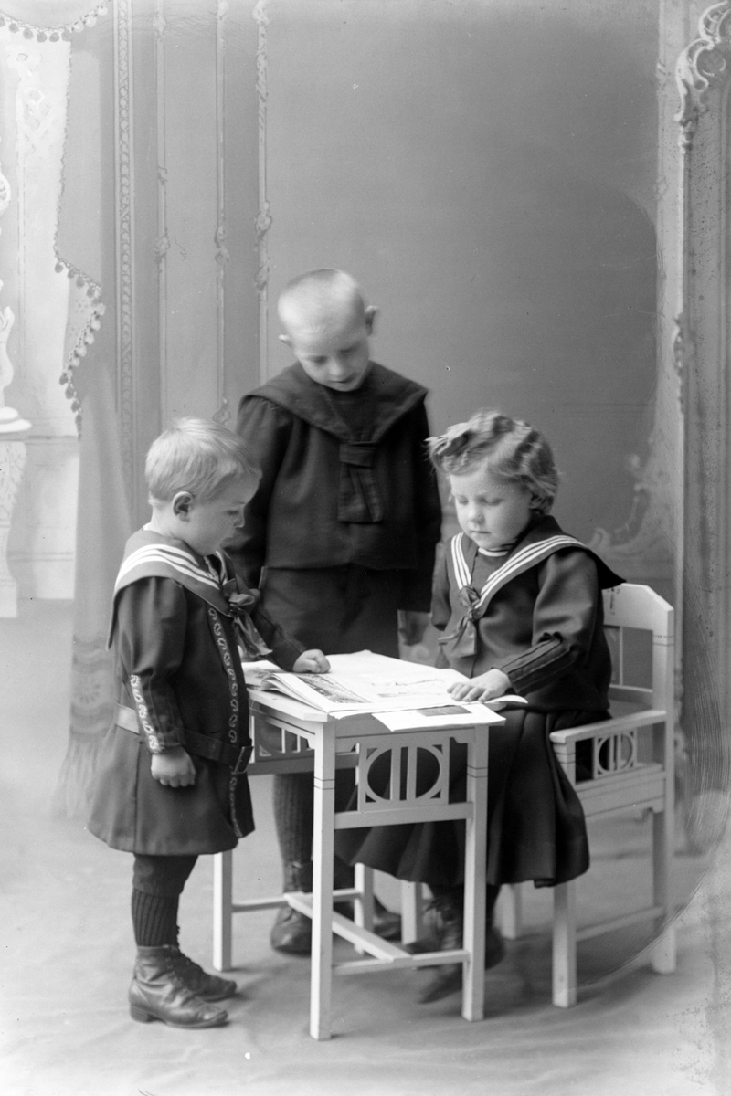 Studioportrett av tre barn samlet rundt et bord.