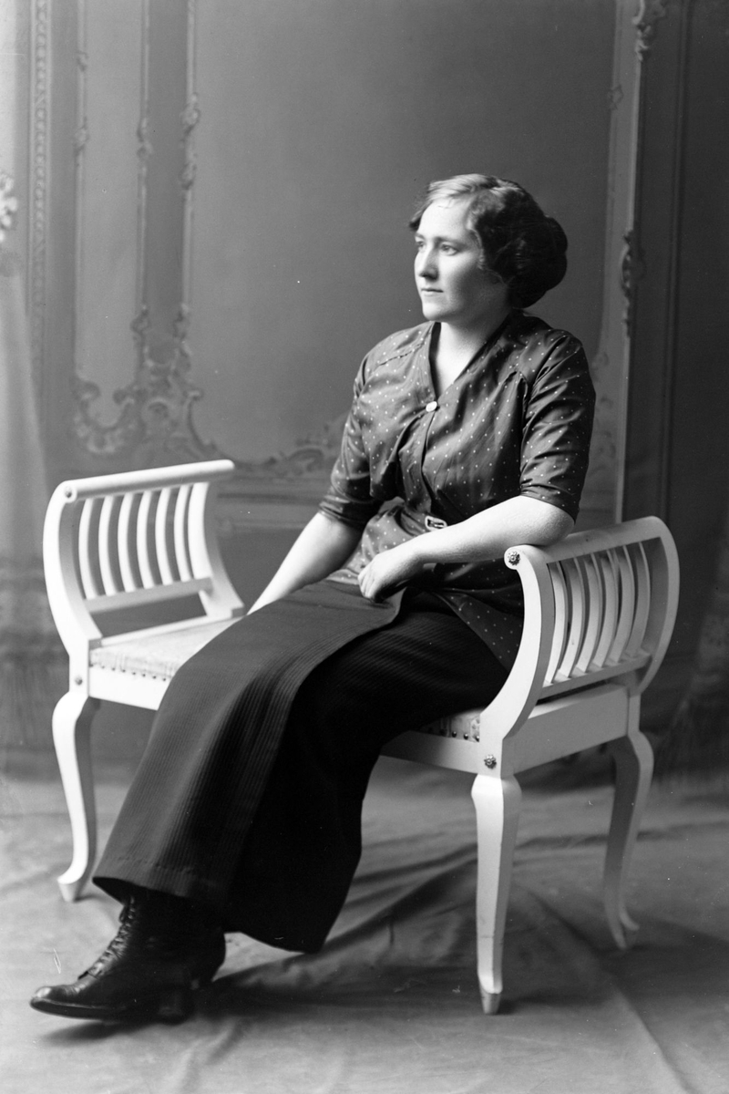 Studioportrett av en kvinne sittende på en hvit benk.