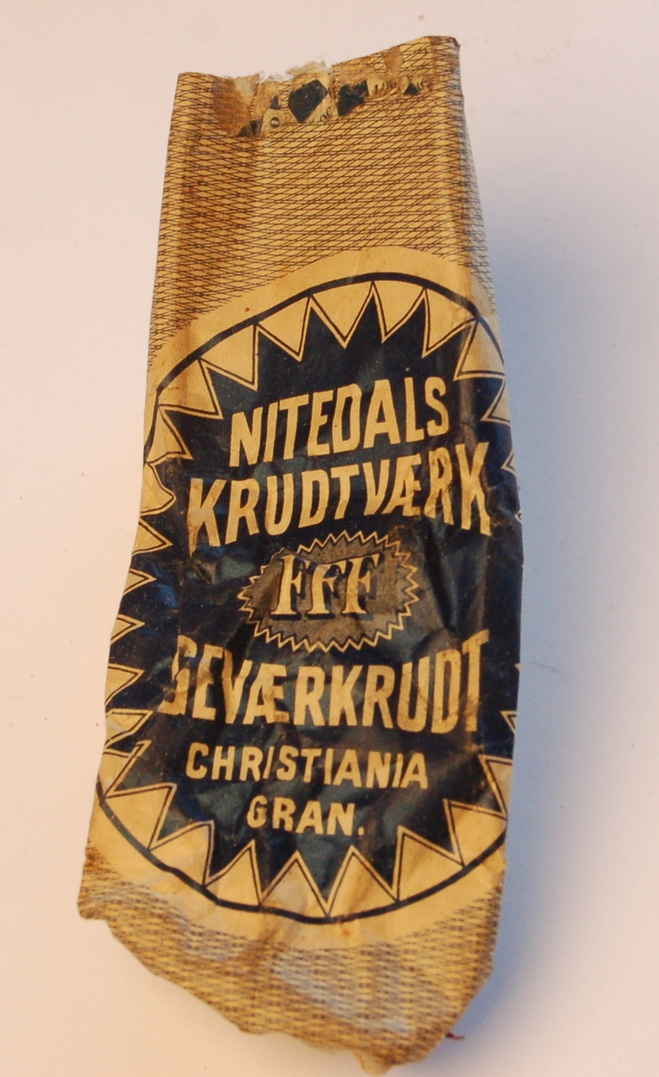 Gjenstanden er en kruttpose levert fra produsent. På posen står: Nitedals Krudtværk Geværkrudt Christiania Gran. Initialer: FFF