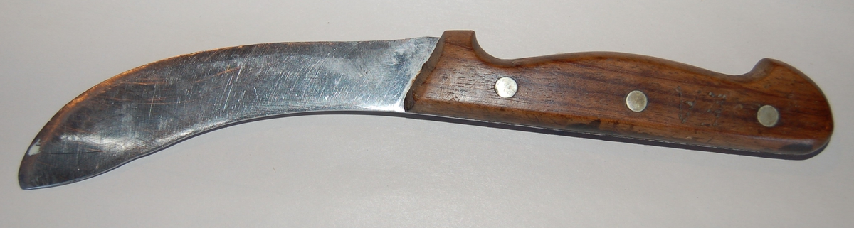 Svakt krummet breitt knivblad med skaft av tre. Skjeftet er festet til knivbladet med 3 messingnagler.