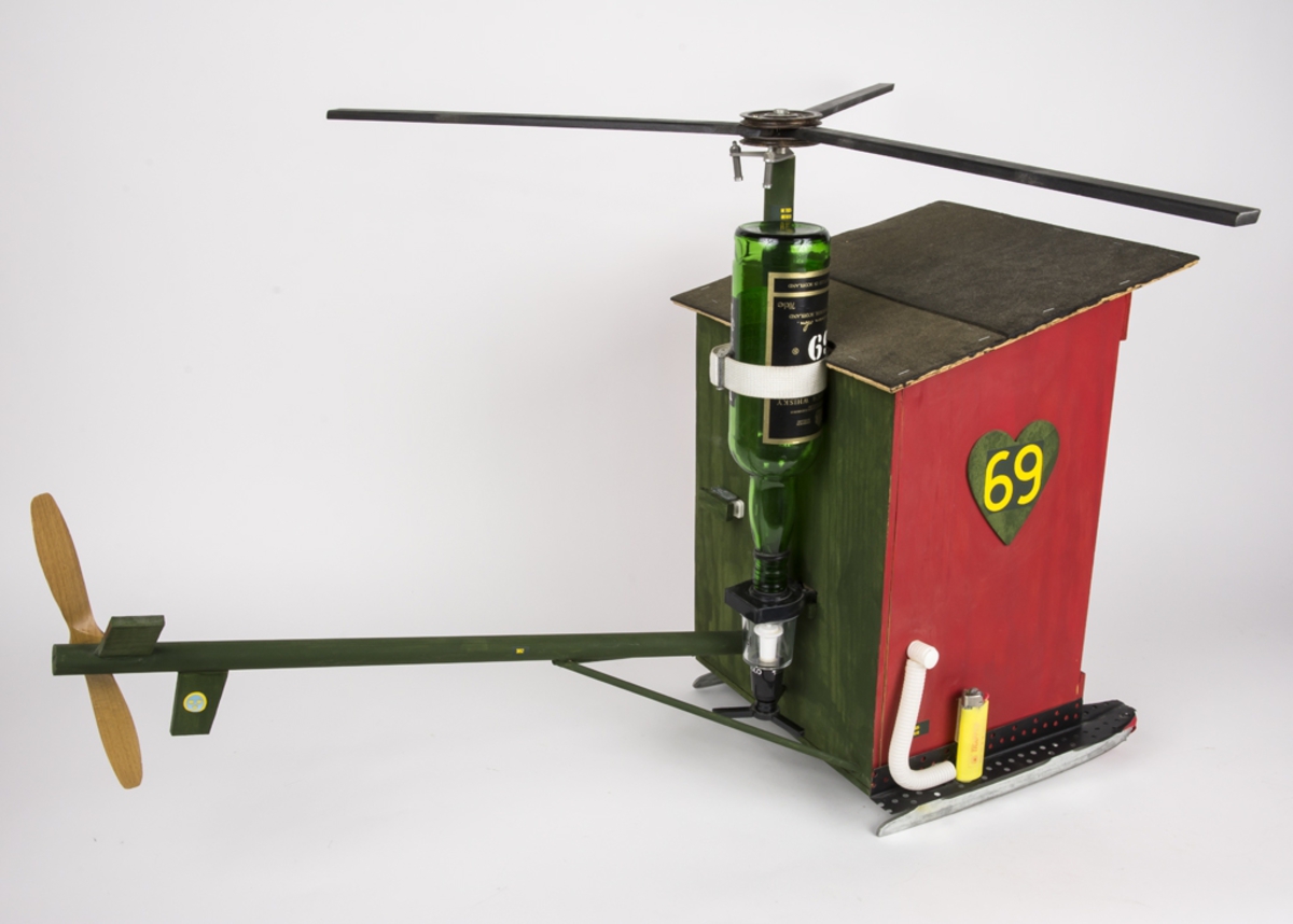 Elevarbete från helikopterutbildningen vid AF2 Malmen. "Pisskuren" förfärdigad av 1995 års GHU-V/G. Tillverkad av trä i lådfom, på skridskor. Ett utedass med docka - som även föreställer en helikopter.