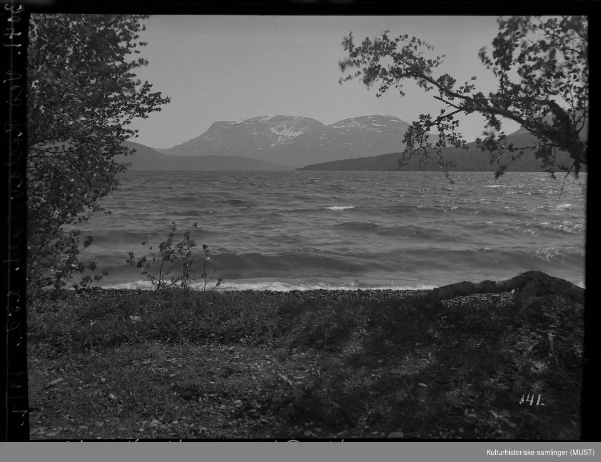 Fotografiet er tatt fra en strand ved Rostavatn i Troms. Fjell i bakgrunnen.