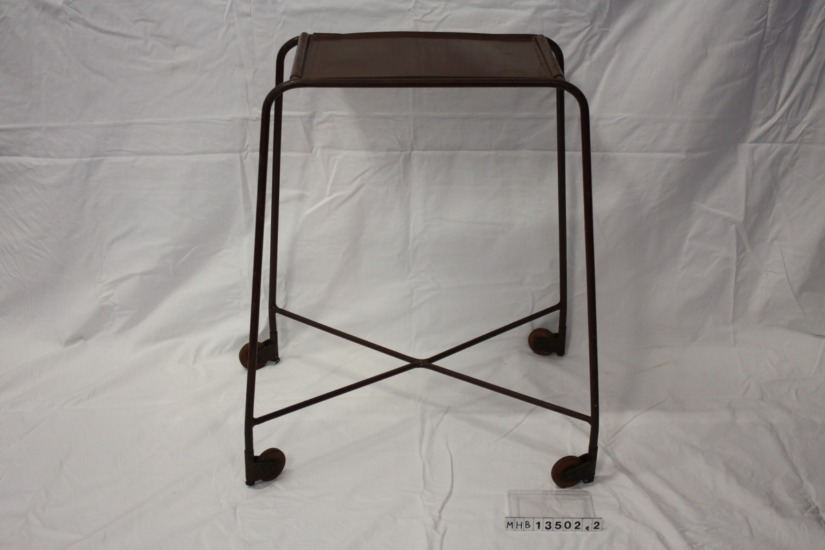 Lite bord med fire høye bein på hjul. Et kryss av stålstenger går nederst mellom beina.