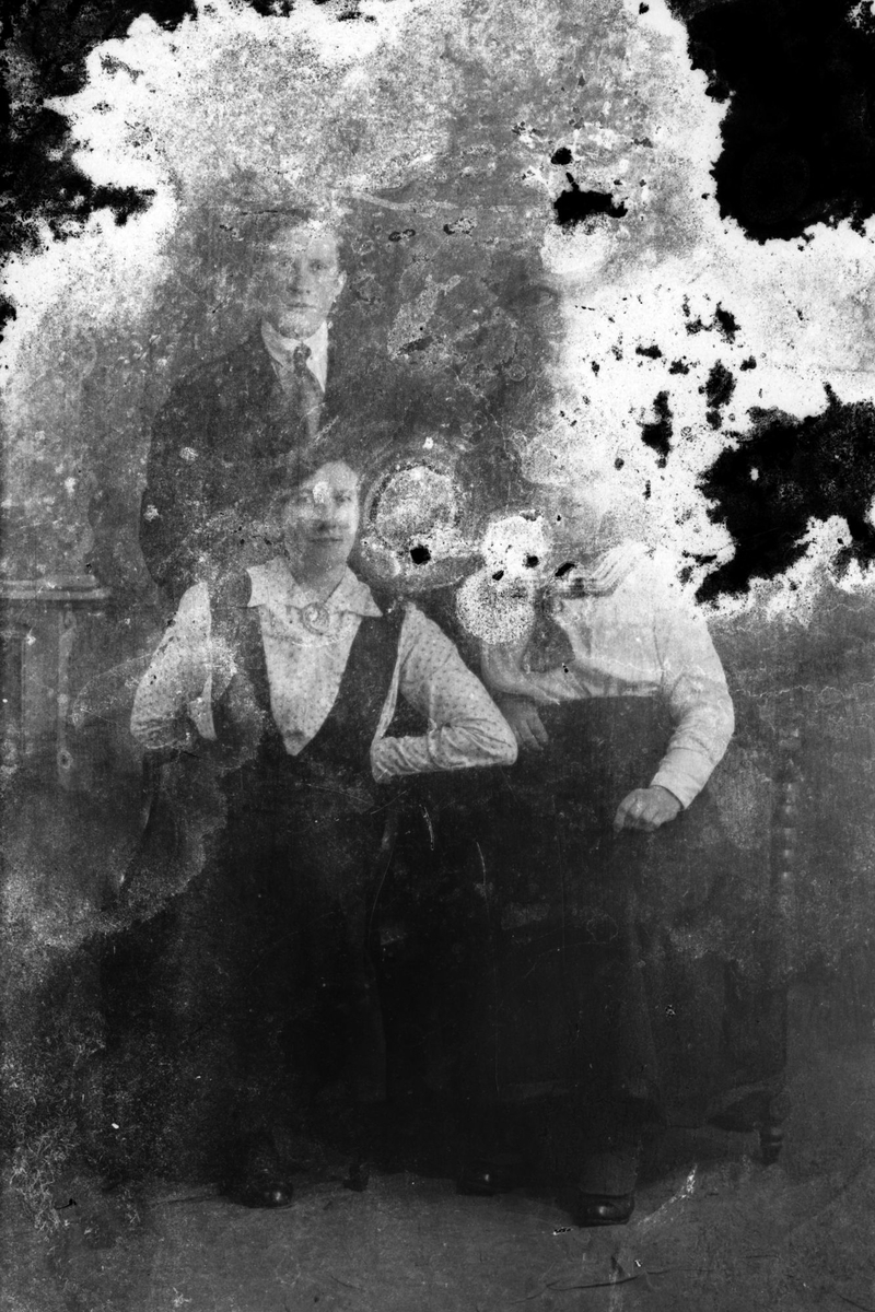Studioportrett av tre personer i helfigur. Bildet er ganske ødelagt.