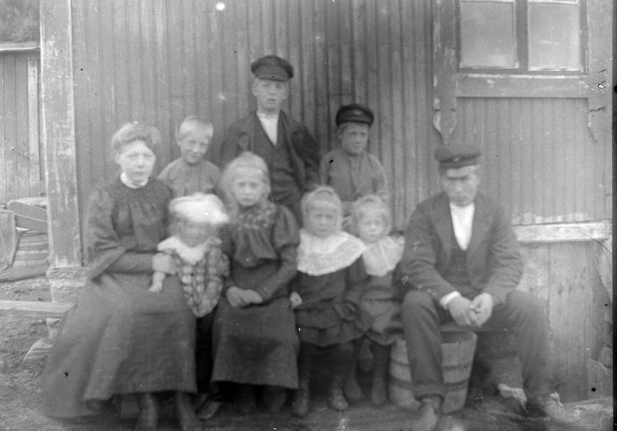 Gruppebilde av en mann og en kvinne med syv barn, foran en husvegg.