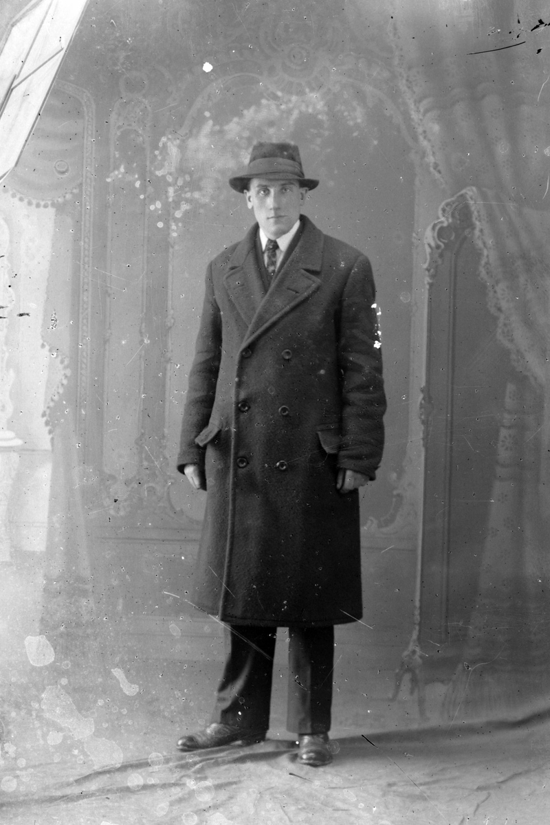Studioportrett av en mann med hatt og frakk.