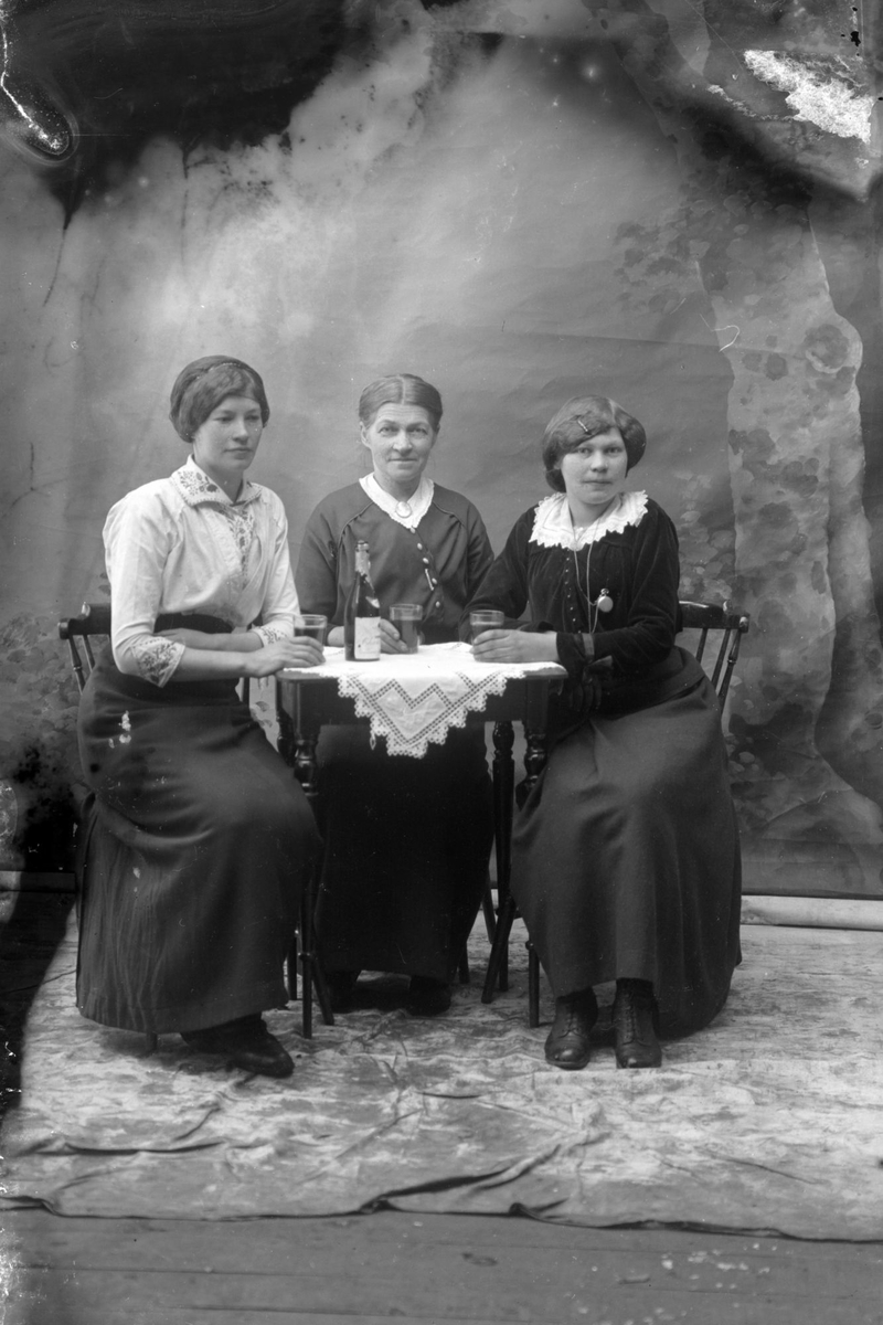 Studioportrett av tre kvinner som sitter rundt et bord.