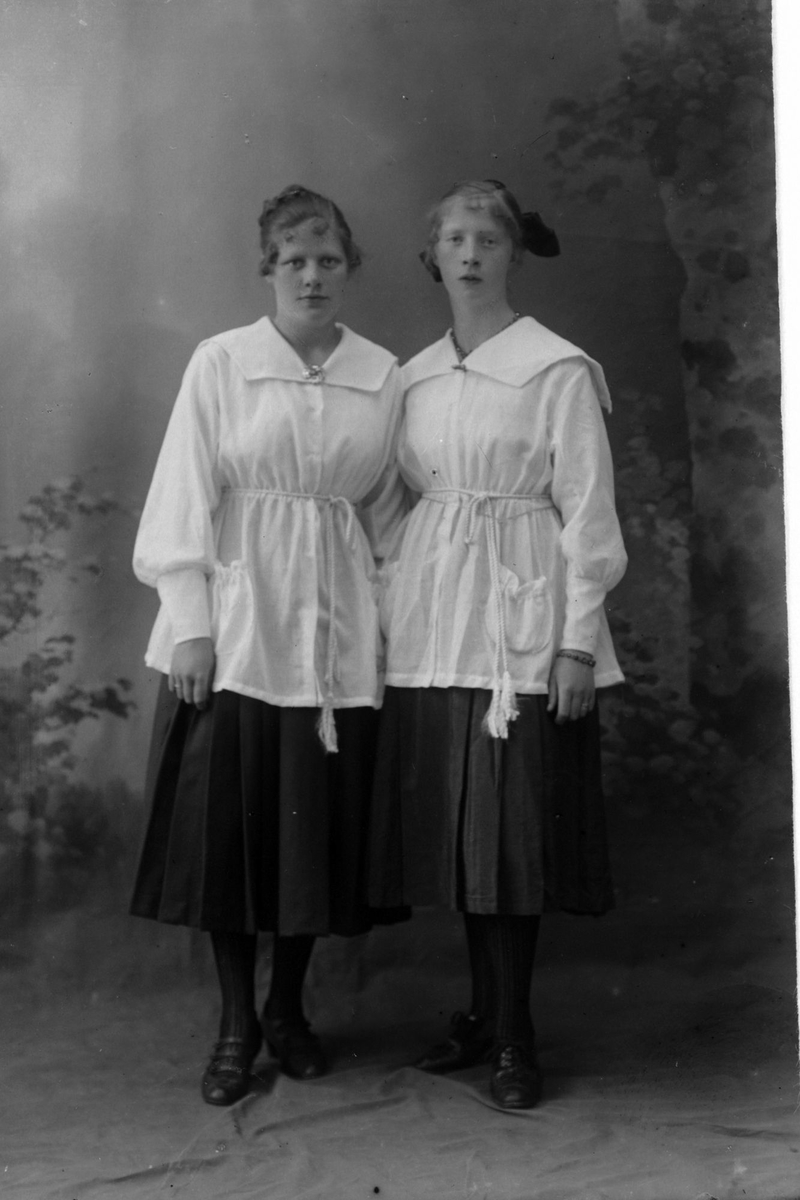 Studioportrett av to kvinner i like klær.