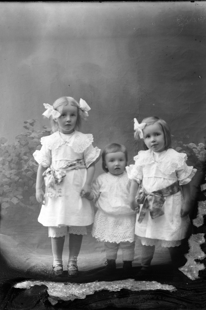 Studioportrett av tre barn kledd i hvite klær.