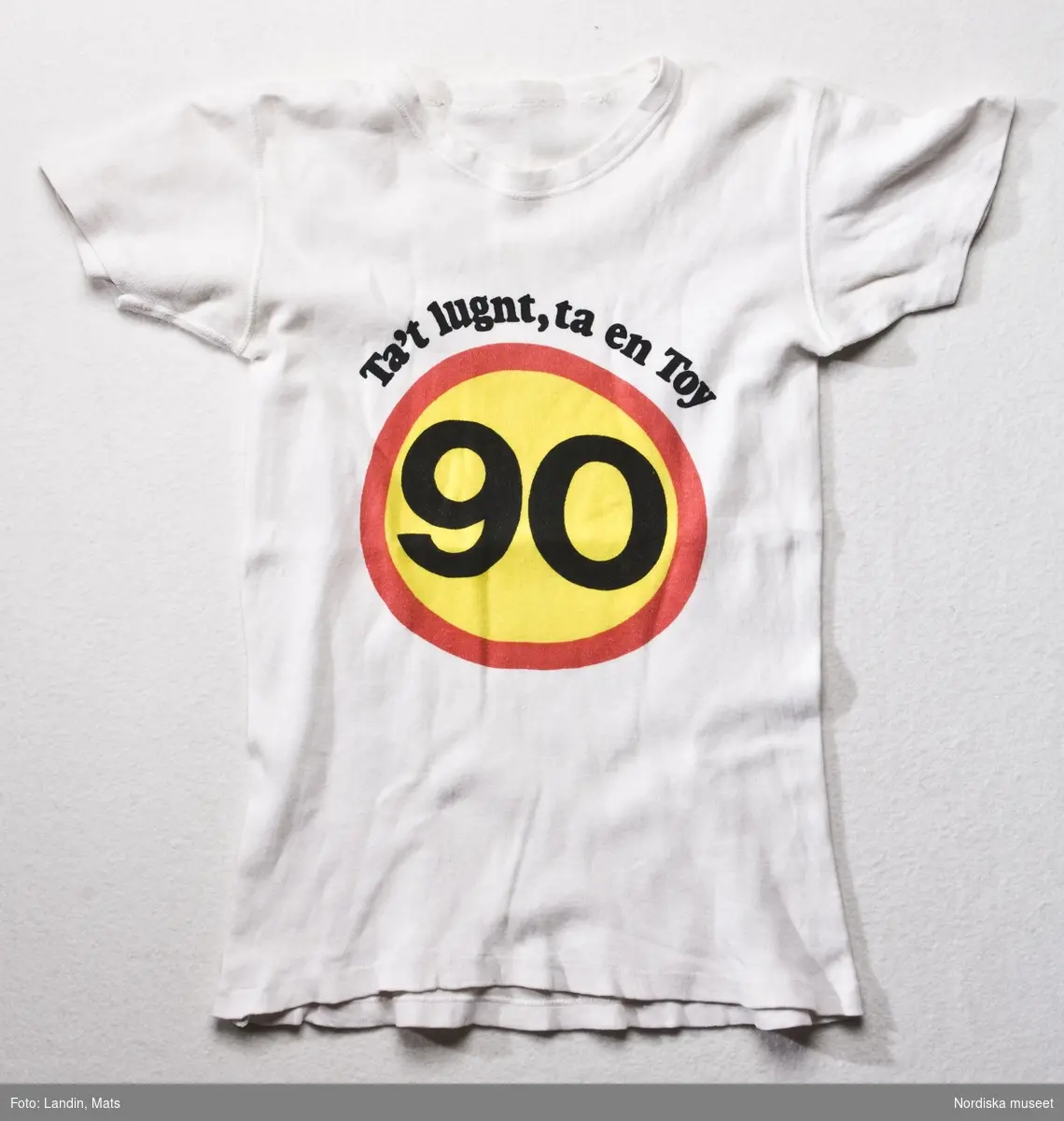 T-shirt med tryck "Ta't lugnt, ta en Toy" och runt trafikmärke med siffran 90.
