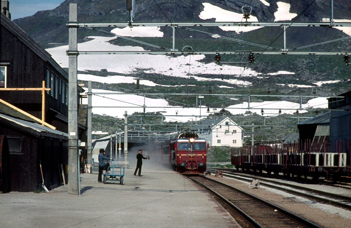 Bergensbanen. Ekspresstog 62 Bergen - Oslo Ø passerer Finse stasjon. Lokomotiv type El 14. Togekspeditøren viser signal "Kryssende tog har kommet".
