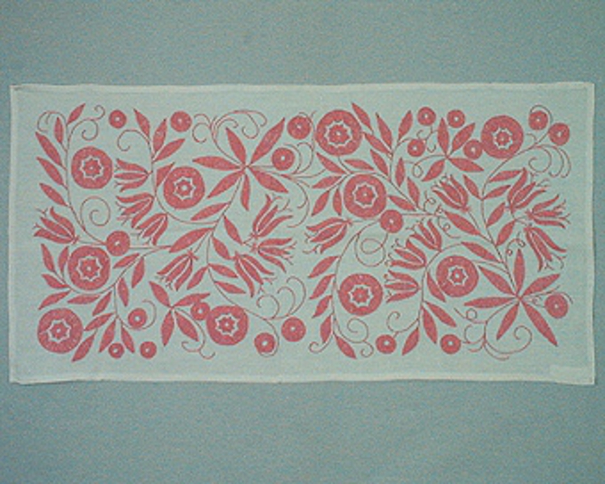 Rektangulär duk i vitt linne broderad i Melpasöm med rosa bomullsgarn.
Duken är fylld med slingor i stjälkstygn med blommor och blad i flätsöm.

Detaljerad beskrivning finns i broderiregistret (kartotek)