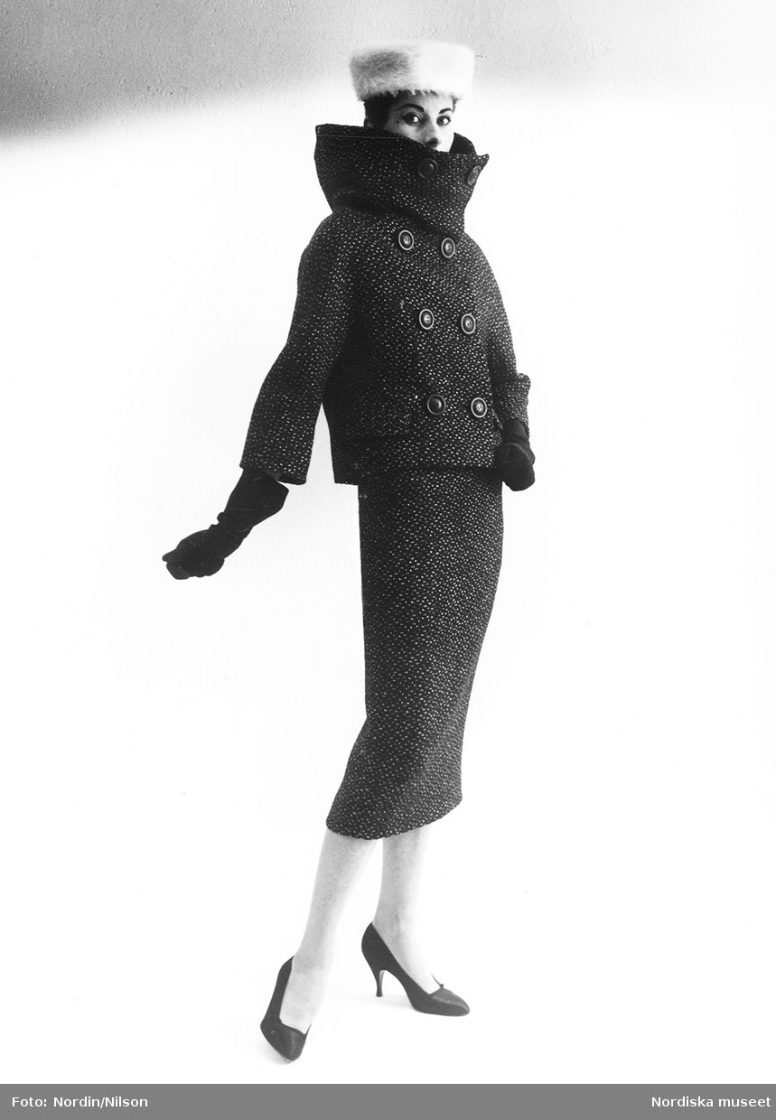 Mannekängen Erika Sundt i tweeddräkt med hög krage, skorstenskrage, handskar, pumps och vit pälshatt. Original från Hubert de Givenchy, NK:s Franska damskrädderi, hösten 1956.