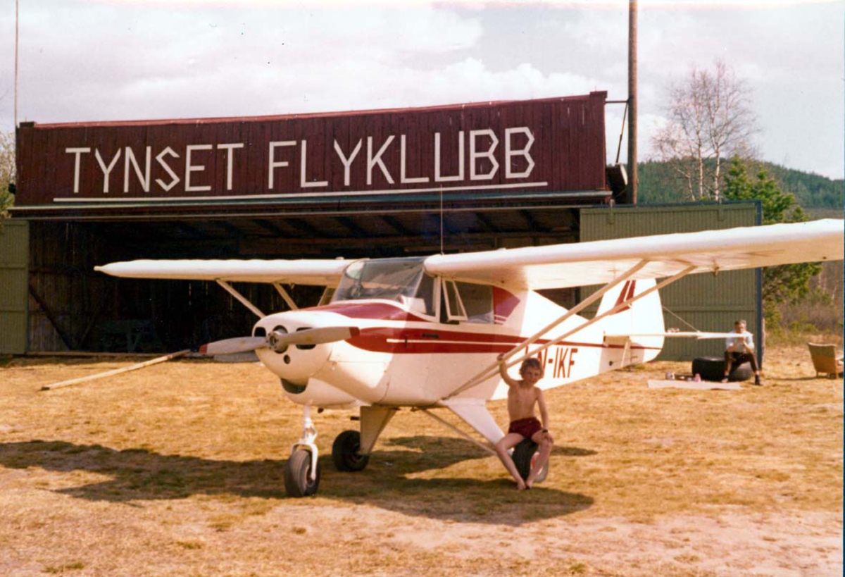 1 fly på bakken, Piper Colt PA-22 LN-IKF. I bakgrunnen bygning med skilt - påskrift "Tynset flyklubb