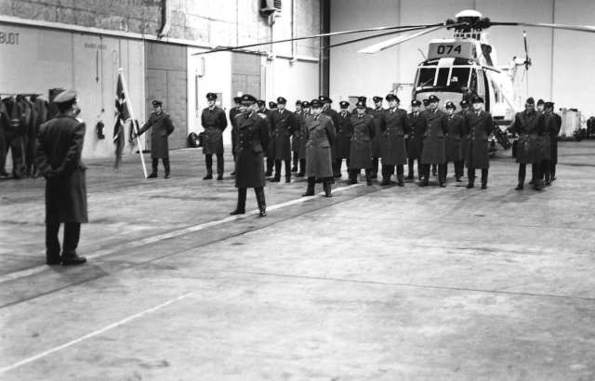 Flere personer på oppstilling i en hangar. I bakgrunnen sees et helikopter.