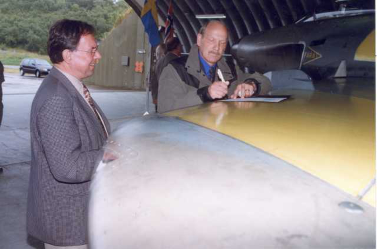 Lufthavn (flyplass). To personer, menn, undertegner en kontrakt/avtale på vingen til en SAAB J-32B Lansen , toseter.