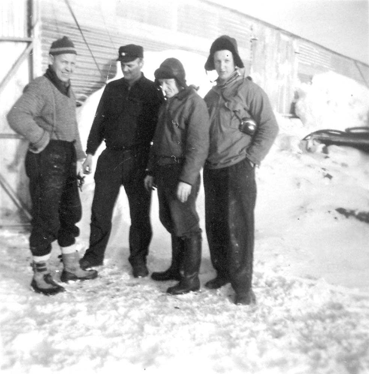 Fire personer som står foran en bygning, menn. Snø på bakken.