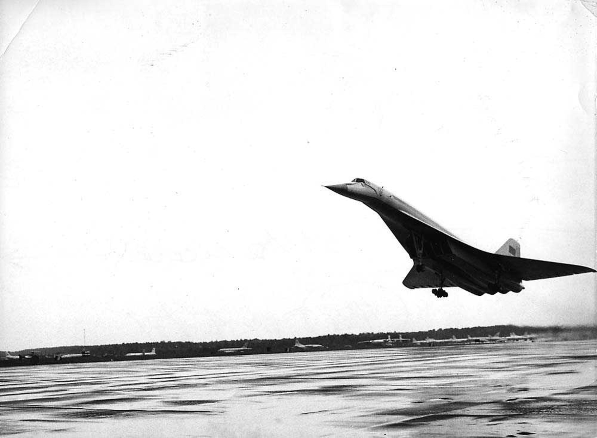 Lufthavn. Ett fly i luften rett før landing/etter take-off, Tupolev Tu-144 Charger. Flere fly på bakken i bakgrunnen.