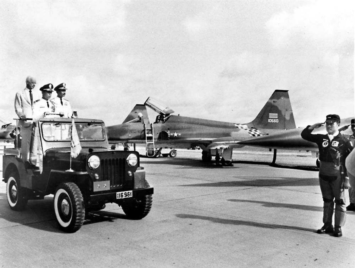 Lufthavn. Ett fly på bakken, Northrop F-5 A/B Freedom Fighter. Flere personer  foran flyet, tre står på en bil.