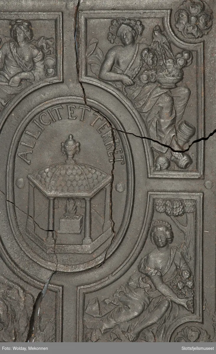 På begge sider, bladkrans. Midt på, et ovalt felt med alter og ild. Rundt feltets overkant er det en innskrift: "Allicit et terret". Rundt midtfeltet er det 4 firkantede felt med allegoriske figurer. Under er innskriften "Anno 1707".