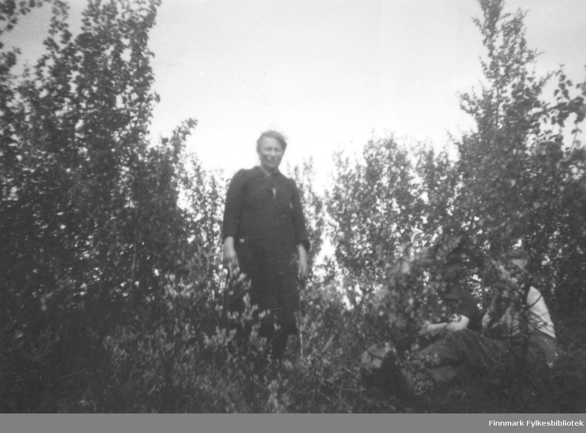 Elen Aslaksen som står inni et kratt på plassen Ruselv i Kokelv. Hun er kledt i en mørk kjole. Det sitter flere personer på bakken