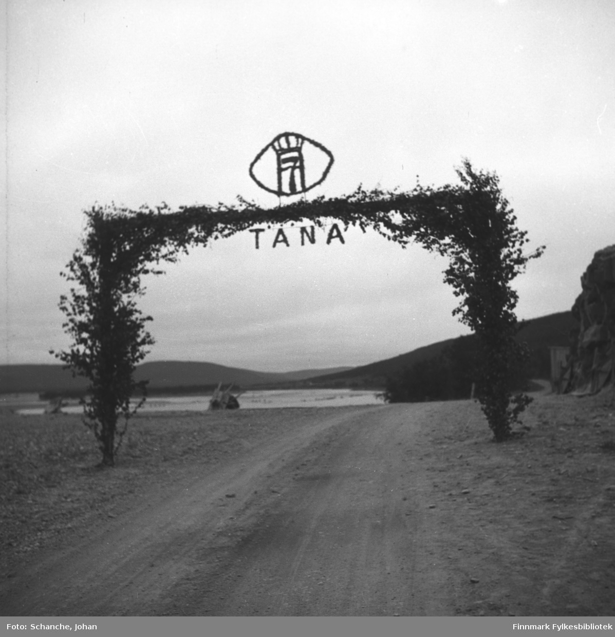 Kongebesøk i 1946, Kong Haakon VII besøker Tana. Kongen reiste fra Vadsø og stoppet i Vestre Jakobselv, Nyborgmoen, Skippagurra og Langnes der han spiste aftens- laks og rabarbragrøt. Vi ser bjørkeportalen (porten) over veien i Tana. Øverst på bjørkeportalen står ordet TANA og Tanas våpen. Vi ser Tanaelva i bakgrunnen.