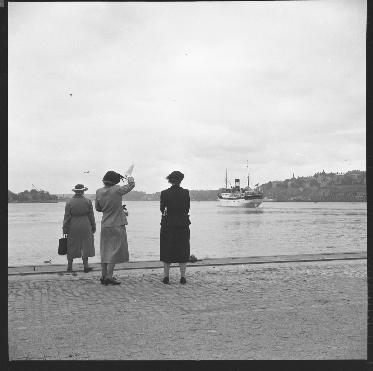 Tre kvinnor vinkar av en båt från Skeppsbrokajen i Stockholm.