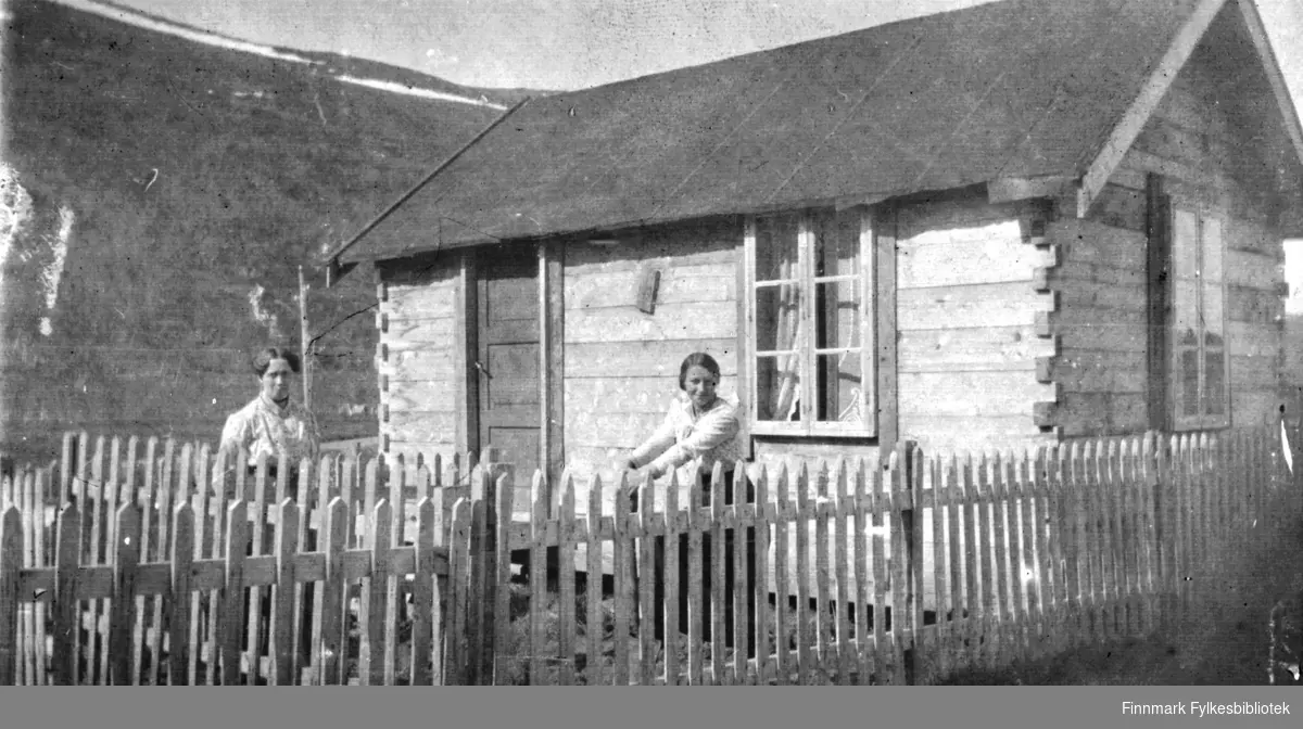 To kvinner utenfor et lite, laftet tømmerhus på langnes i Tana