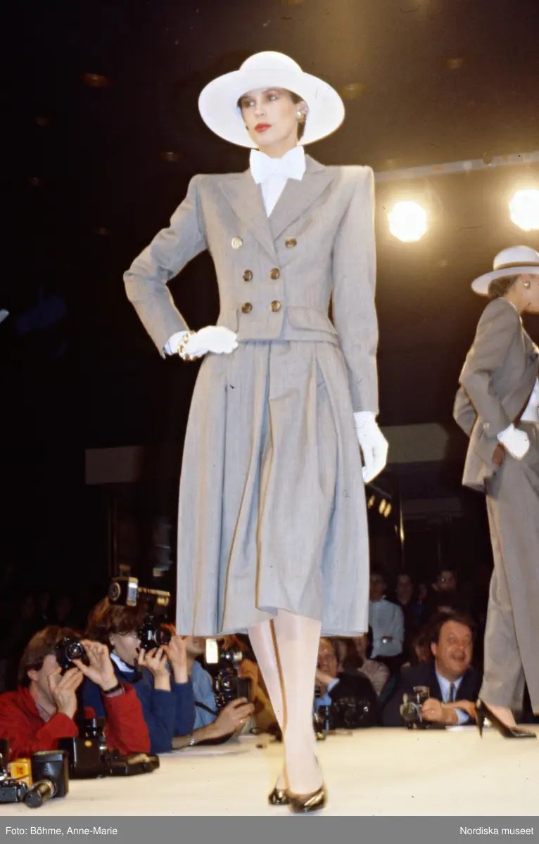 Modevisning. Modell i grå dräkt, vit fluga, hatt och handskar. Från ...