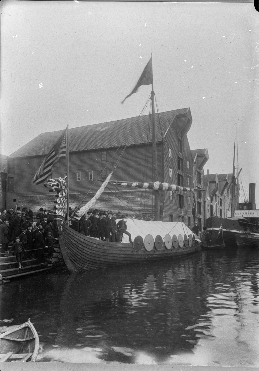 Vikingskipet "Leif Erikson" ved kai i Haugesund. Personer ombord på skipet og på kaien. Sjøhus, og dampskipet D/S "Alexander" i bakgrunnen.
