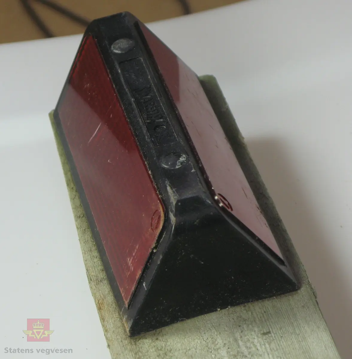 Viltspeil som består av rød refleks med svart omramming, lagd av plast. Festet til toppen av en stolpe, lagd av impregnert tre, spisset i enden. Stolpen er kuttet på langs slik at den utgjør halvparten av en sylindrisk stolpe. Merking fra produsent.