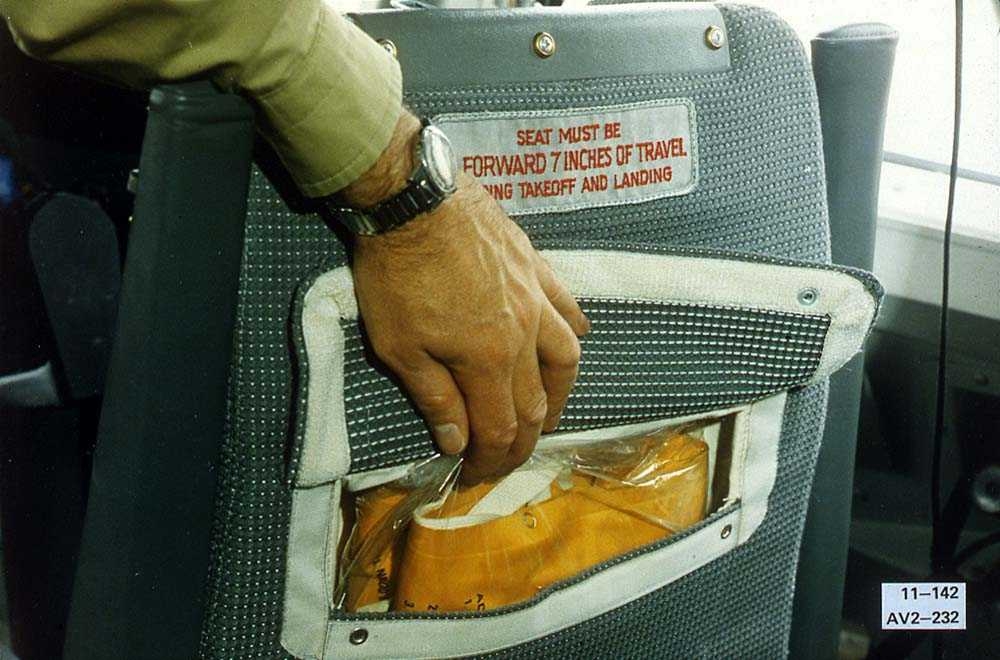Detaljbilde av baksiden på en stol ombord i et fly, med en redningsvest i stollommen. 