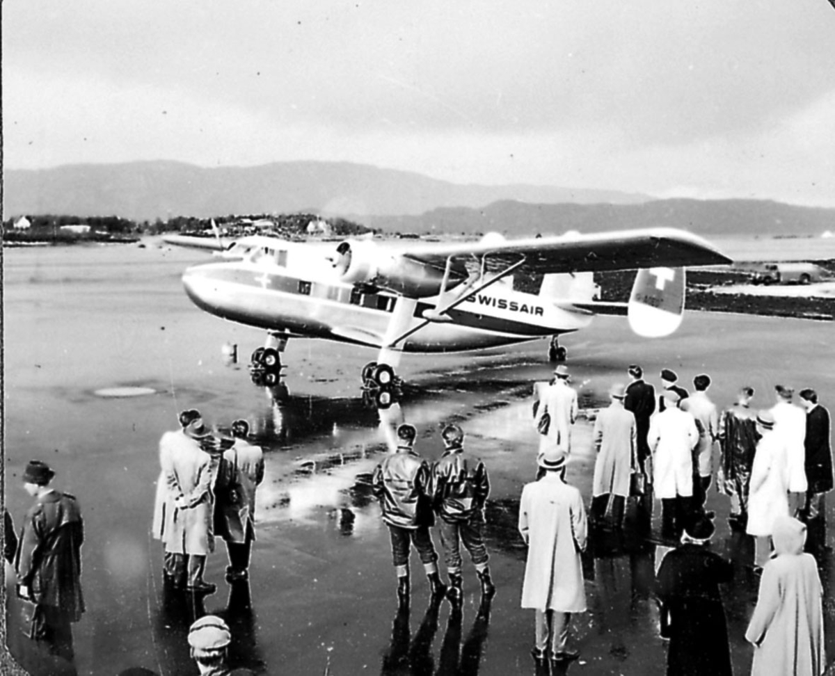 Lufthavn (flyplass).  Ett fly på bakken, Scottish Aviation Twin Pioneer  fra SWISSAIR. Flere personer - passasjerer ved flyet.
