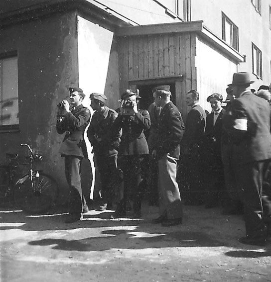 Frigjøringsdagene i Bodø etter krigen  1945. Noen militære og sivile personer foran bygning. Noen med fotoapparat.