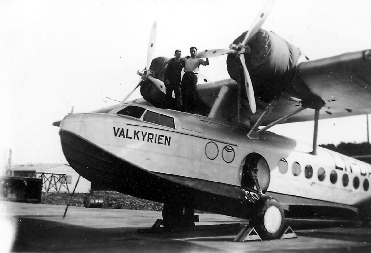 Åpen plass, ant. lufthavn. ett fly på bakken, Sikorsky S.43, LN-DAG "Valkyrien". to personer står oppe på flyet.