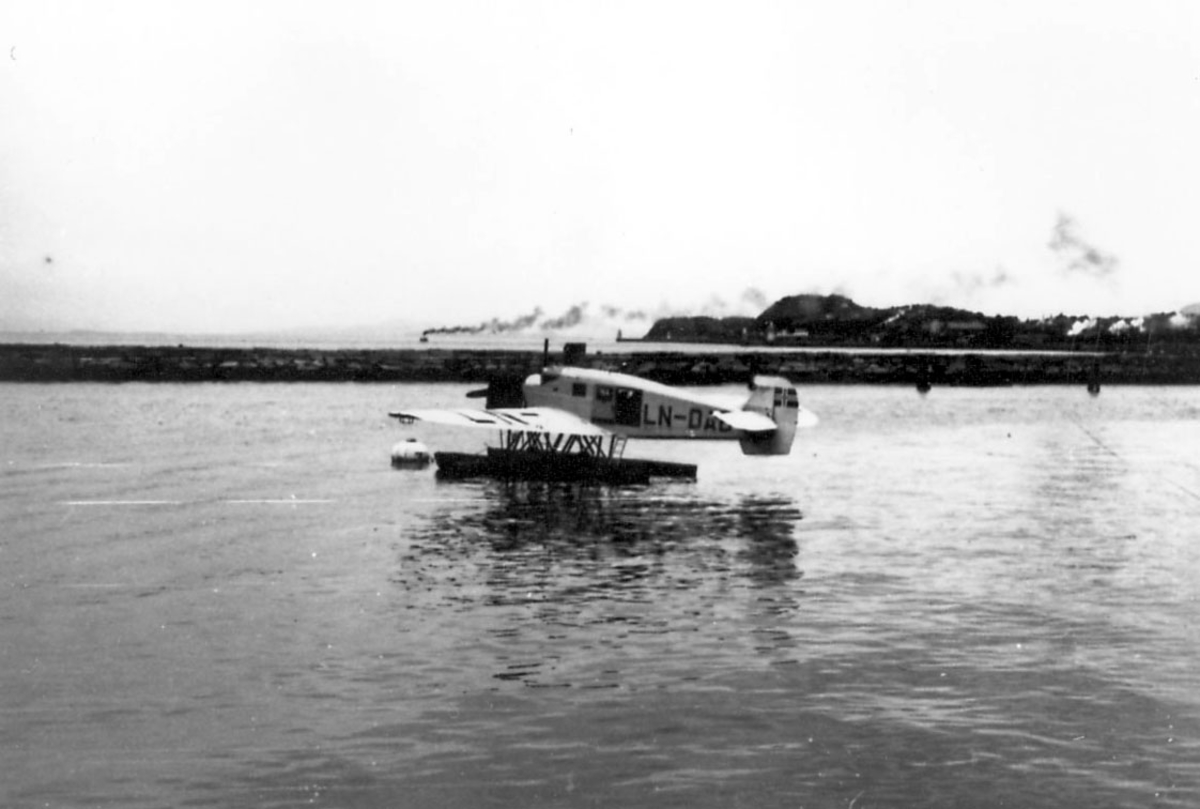 Ett fly på vannet, Junkers Ju W 34 LN-DAB  "Ternen", fortøyd i bøye. Bebyggelse inne på land bak.