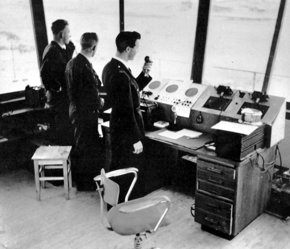 Bodø lufthavn. Portrett, tre personer, en flygeleder, en militær liaison offiser og en flygelederassistent, ved kontrollpulten i det gamle flytårnet. (1952).