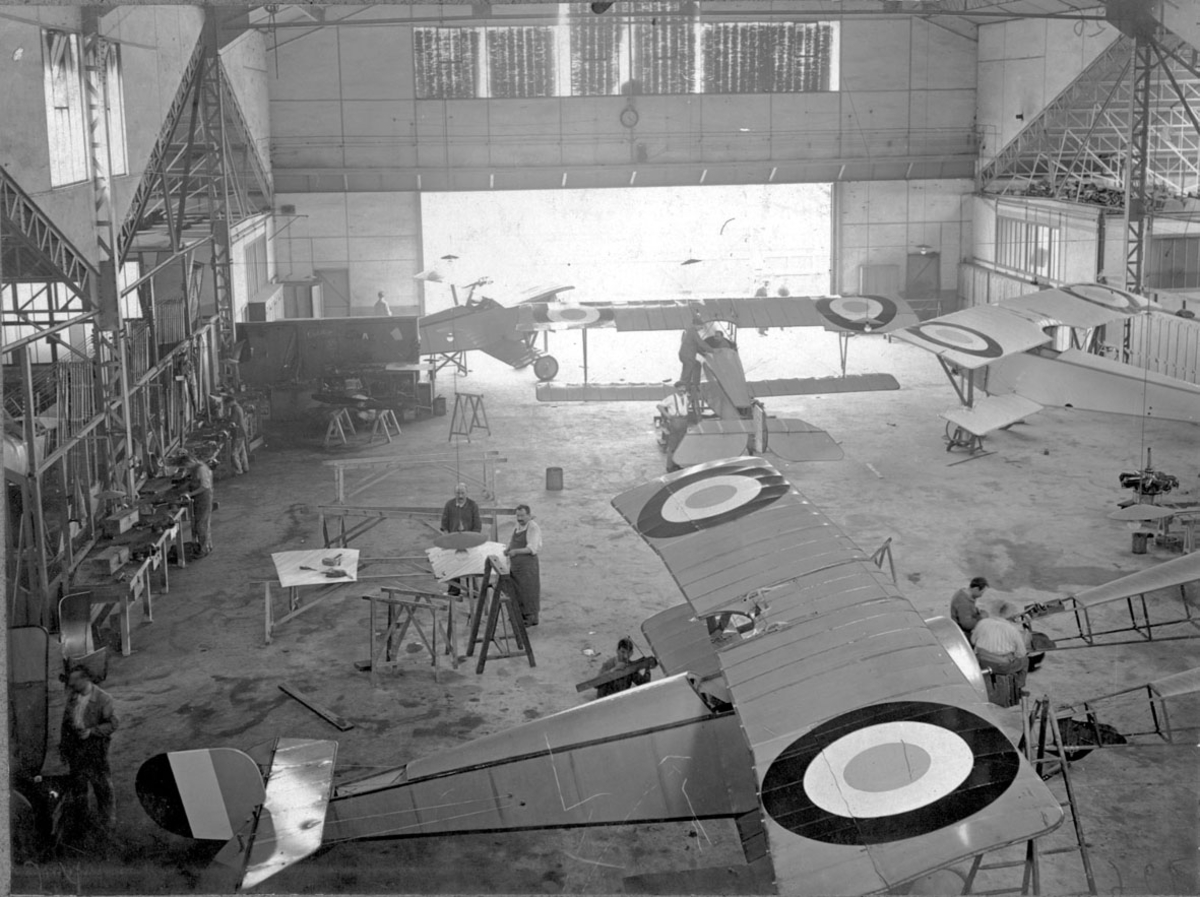 Fly, 4 stk. Nieuport 11C.1, inne i hangar. Sett ovenfra. Flere personer arbeider med flyene. 