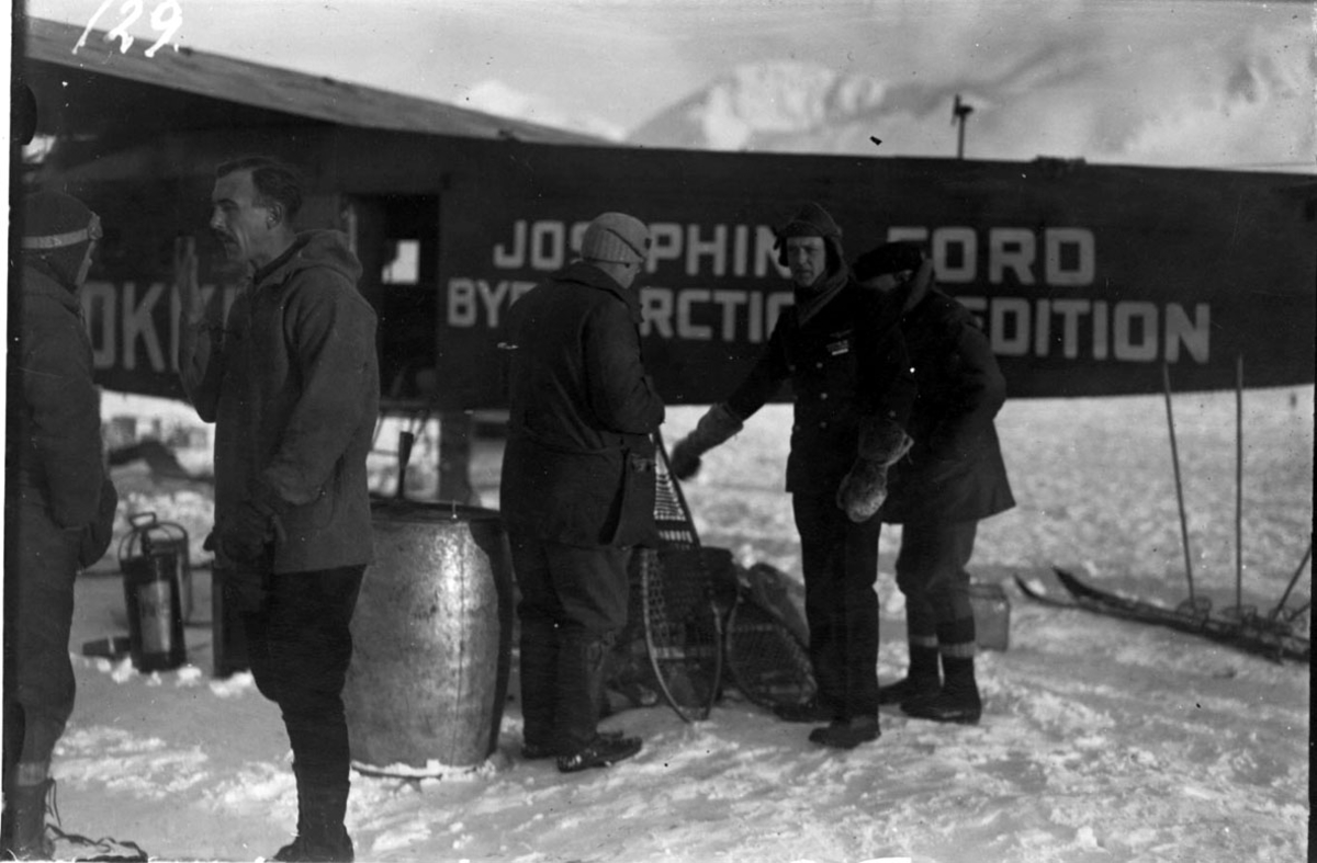 4 personer i forgrunnen + flygere. Fly, bak, Fokker FVII "Josephine Ford". En del utstyr på bakken som lastes inn i flyet. Snø på bakken.